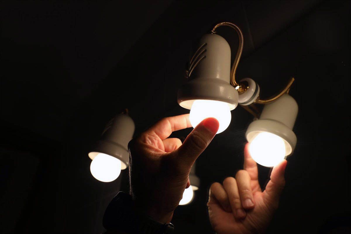 Una persona ajusta una bombilla de una lámpara eléctrica. Precio la luz / Foto: EP