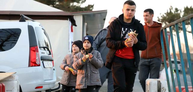 Un adolescente y dos niños caminan mientras comen unos bocadillos que les han brindado en una de las muchas carpas de servicios en Siret (Rumanía) / Foto: FFM - EA