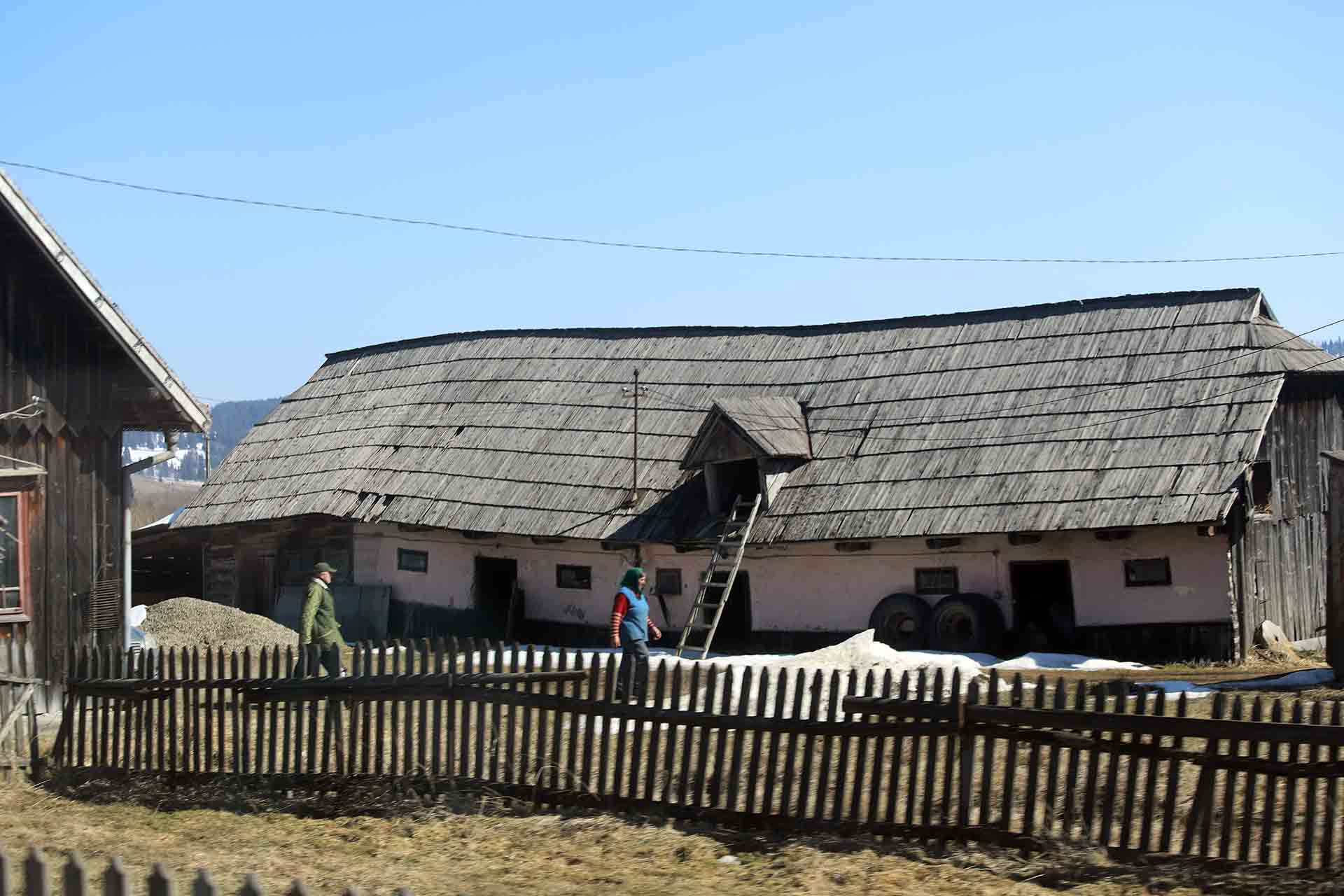 Dos persones mayores junto a lo que se asemeja a una antigua granja estatal / Foto: FFM - EA