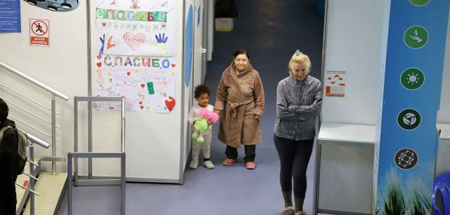 Dos mujeres y una niña contemplan como juegan otras niñas y niños ucranianas en el interior de uno de los pabellones de MoldExpo, en Chisináu (Moldavia)  / Foto: FFM - EA