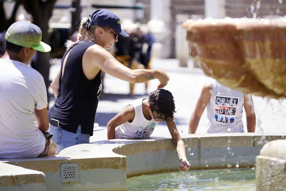 Una madre le echa agua a su hijo, por la cabeza, en la fuente de la plaza Virgen de los Reyes en el primer día de la segunda ola de calor, a 7 de julio de 2022 en Sevilla (Andalucía, España) / Foto: EP