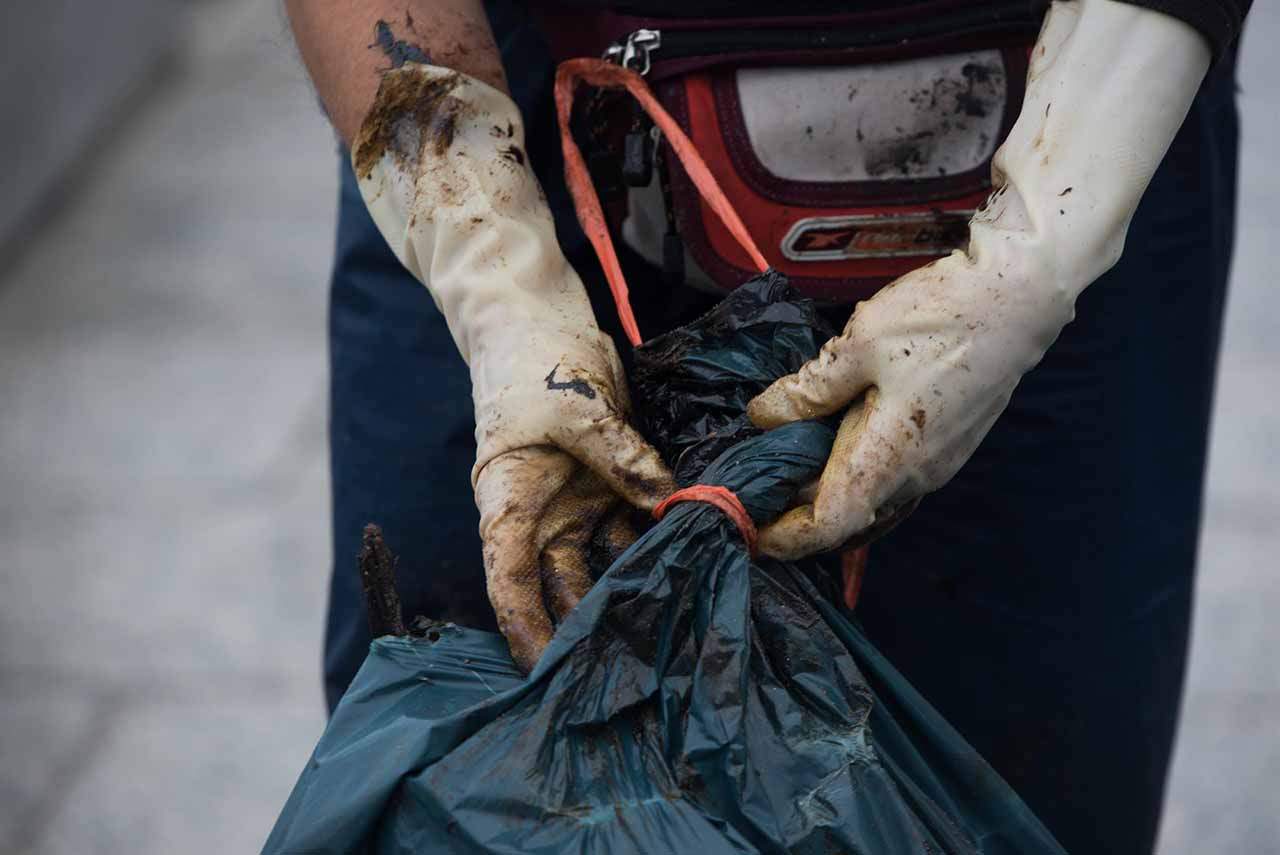 De nuevo, chapapote en A Illa de Arousa. Una mujer cierra una bolsa con los restos de chapapote mezclados con algas recogidos en una playa / Foto: EP