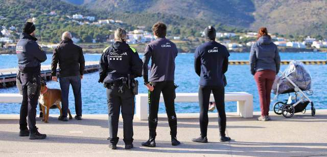 Una miembro de la Guardia Municipal, otro de la Unidad Marítima de los Mossos de Escuadra, técnicos del CRAM y varias personas observan detenidamente el ejemplar de delfín listado en el Moll d’en Balleu en el Port de la Selva en Catalunya (España) / Foto: FFM - EA