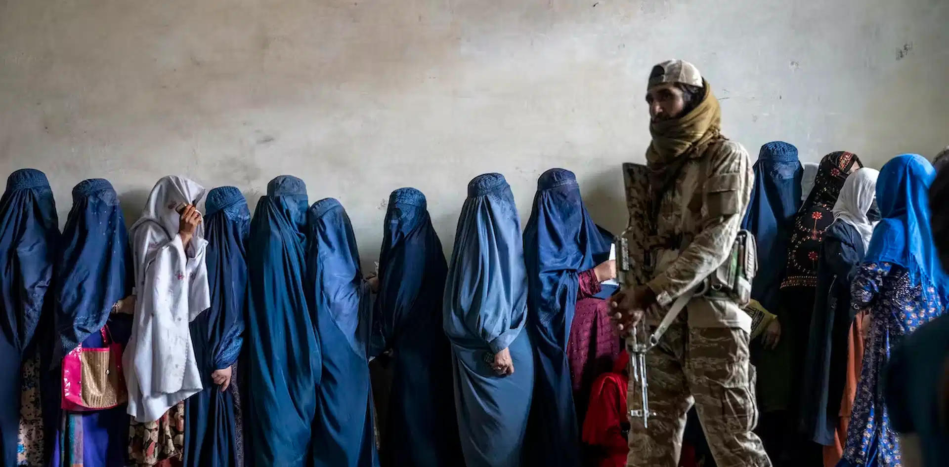 Un combatiente talibán monta guardia mientras unas mujeres esperan para recibir raciones de comida distribuidas por un grupo de ayuda humanitaria, en Kabul, Afganistán, en mayo de 2023 / Foto: The Conversation