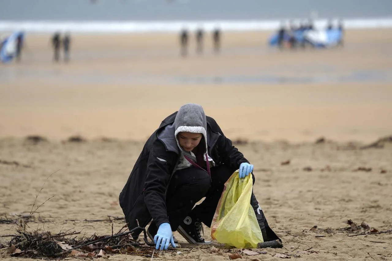 Voluntaria recoge pélets en la playa bajo la lluvia en Gijón. Marea blanca con consecuencias negras / Foto: SINC