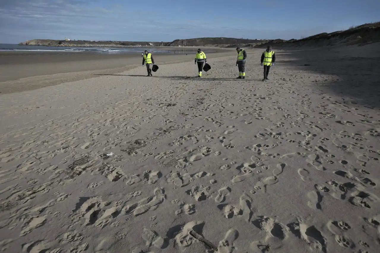 Varios hombres recogen pélets en una playa / Foto: EP
