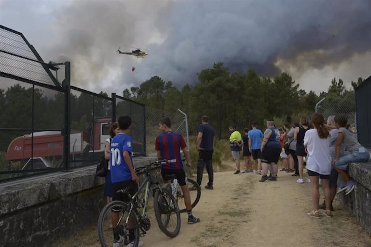 El fuego se extiende por muchos puntos de España. Vecinos observan el fuego, a 12 de agosto de 2025, en Seixalbo, Ourense, Galicia