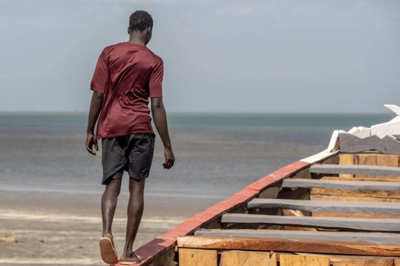 Rastrear desapariciones de migrantes y dar respuestas a sus familias. Joven camina sobre una barca en la costa de Gambia / Foto:  OIM/Lamin Sanneh