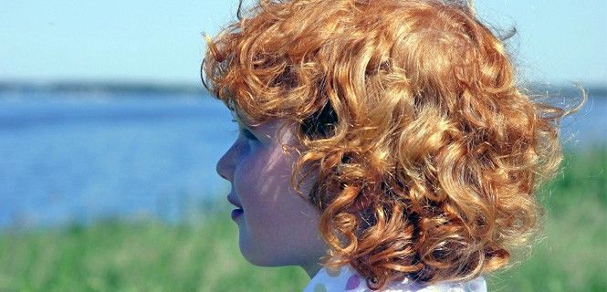 Una niña de cabello rojo y piel clara mirando al mar / Foto: Junglefrog Images
