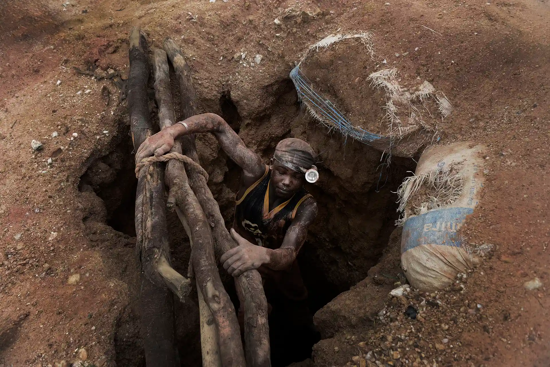 Un minero sube del pozo aferrado a unos troncos la escalera artesanal de una mina sin medidas de seguridad / Foto: Alfons Rodríguez