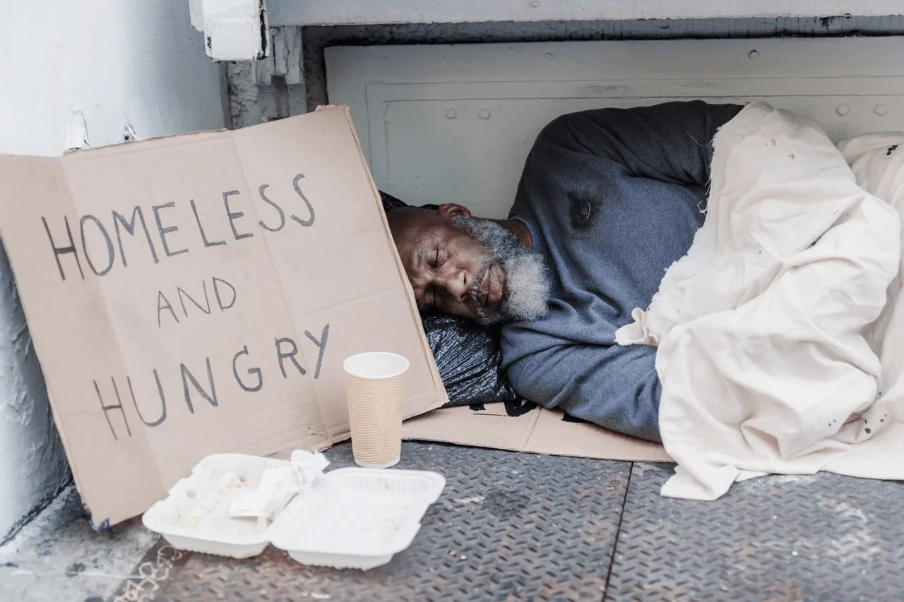 Un hombre sin hogar duerme en la acera junto a un cartel. La mitad de quienes viven sin hogar de forma crónica presenta lesiones cerebrales importantes / Foto: PX Un hombre sin hogar duerme en la acera junto a un cartel. La mitad de quienes viven sin hogar de forma crónica presenta lesiones cerebrales importantes / Foto: PX