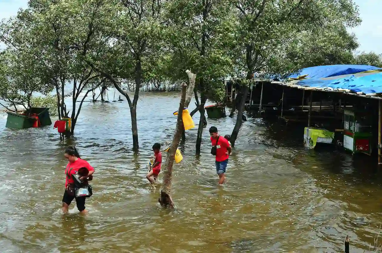 Personas caminan por una costa inundada en el norte de Yakarta, en Indonesia, una de las zonas amenazadas por la subida del nivel del mar / Foto: UP