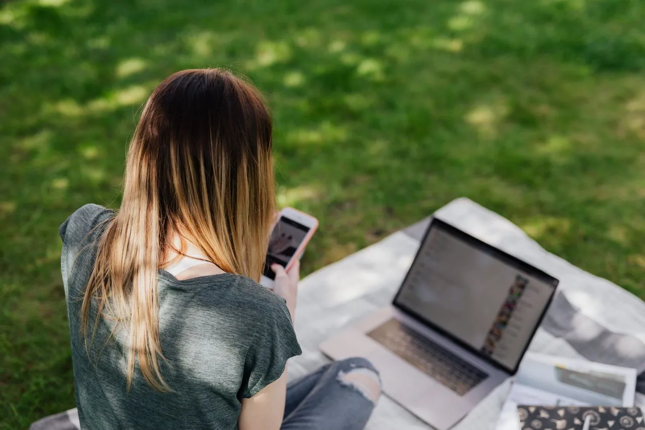 Una adolescente navega por las redes sociales con el móvil y el portátil en un parque; Canadá quiere que las redes demuestren ser seguras antes de abrir cuentas a menores de 16 años / Foto: PX