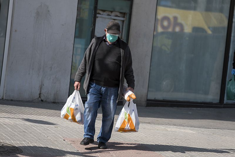 Un vecino confinado regresa de la compra protegiendo su boca y nariz con una mascarilla / Foto: Josep Cano