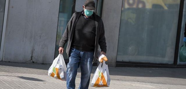 Un vecino confinado regresa de la compra protegiendo su boca y nariz con una mascarilla / Foto: Josep Cano