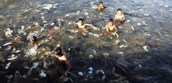Unos niños nadan rodeados de basura y plástico en una playa al norte de Yakarta, Indonesia / Foto: Herianus