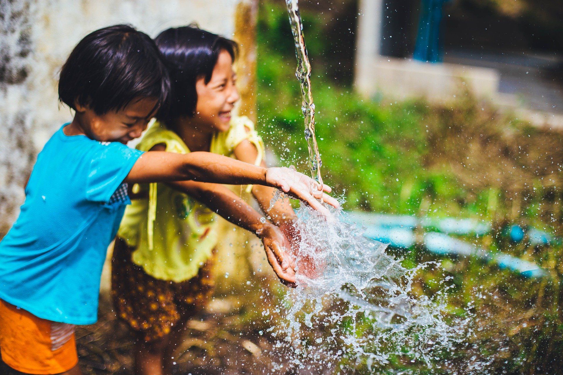 Una niña y un niño juegan bajo un chorro de agua. Día Mundial del Agua / Foto: Pixabay